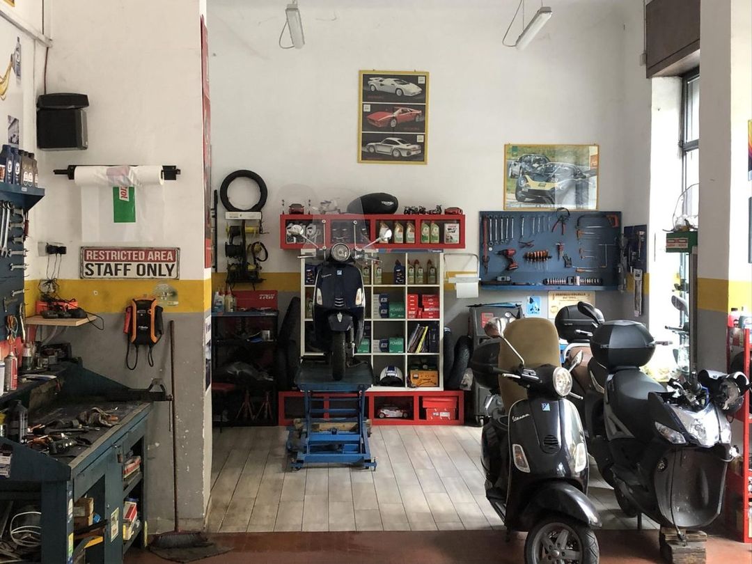 Interno dell'officina Fratelli Colella: banco da lavoro, pannello degli attrezzi, ponte per scooter e scaffali dei lubrificanti